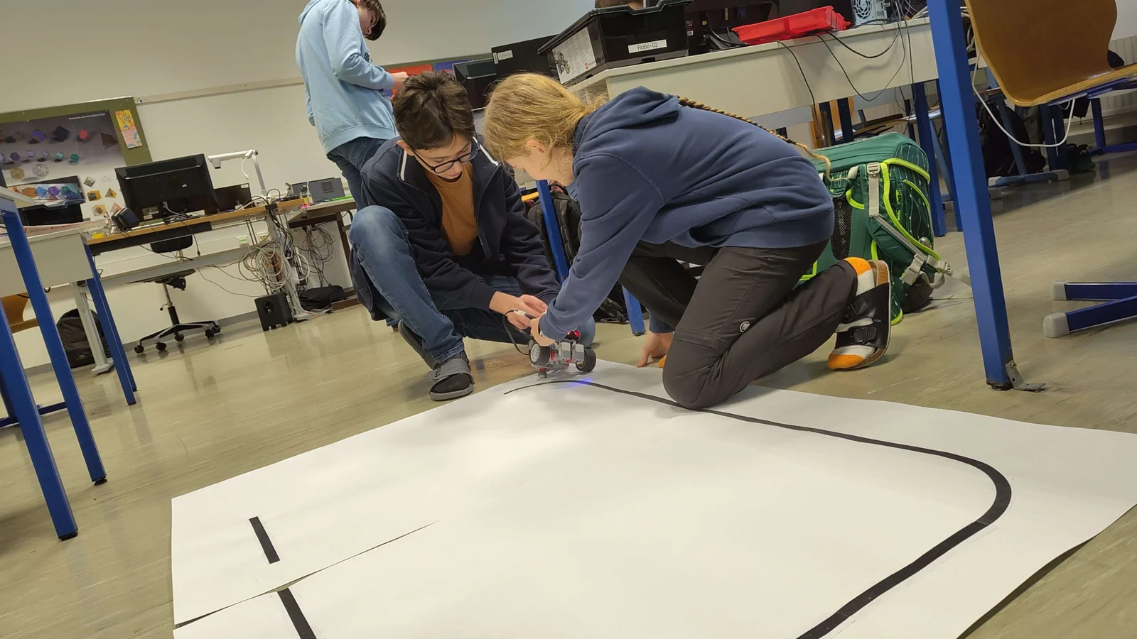 Schüler:innen testen gemeinsam einen Roboter auf einer Fahrstrecke.